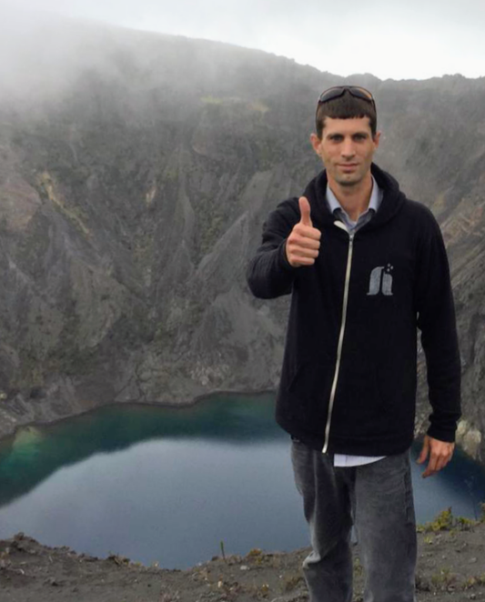 man with thumbs up with lake and mountainside in the background