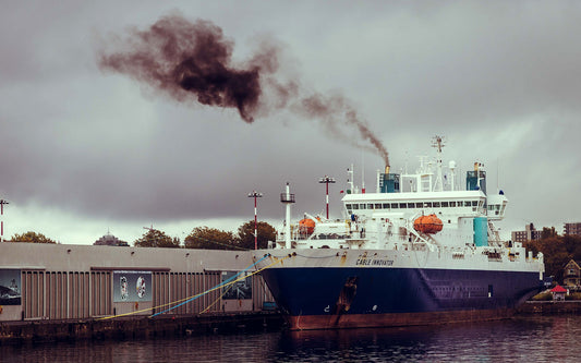 A ship anchored with black smoke coming out its chimney